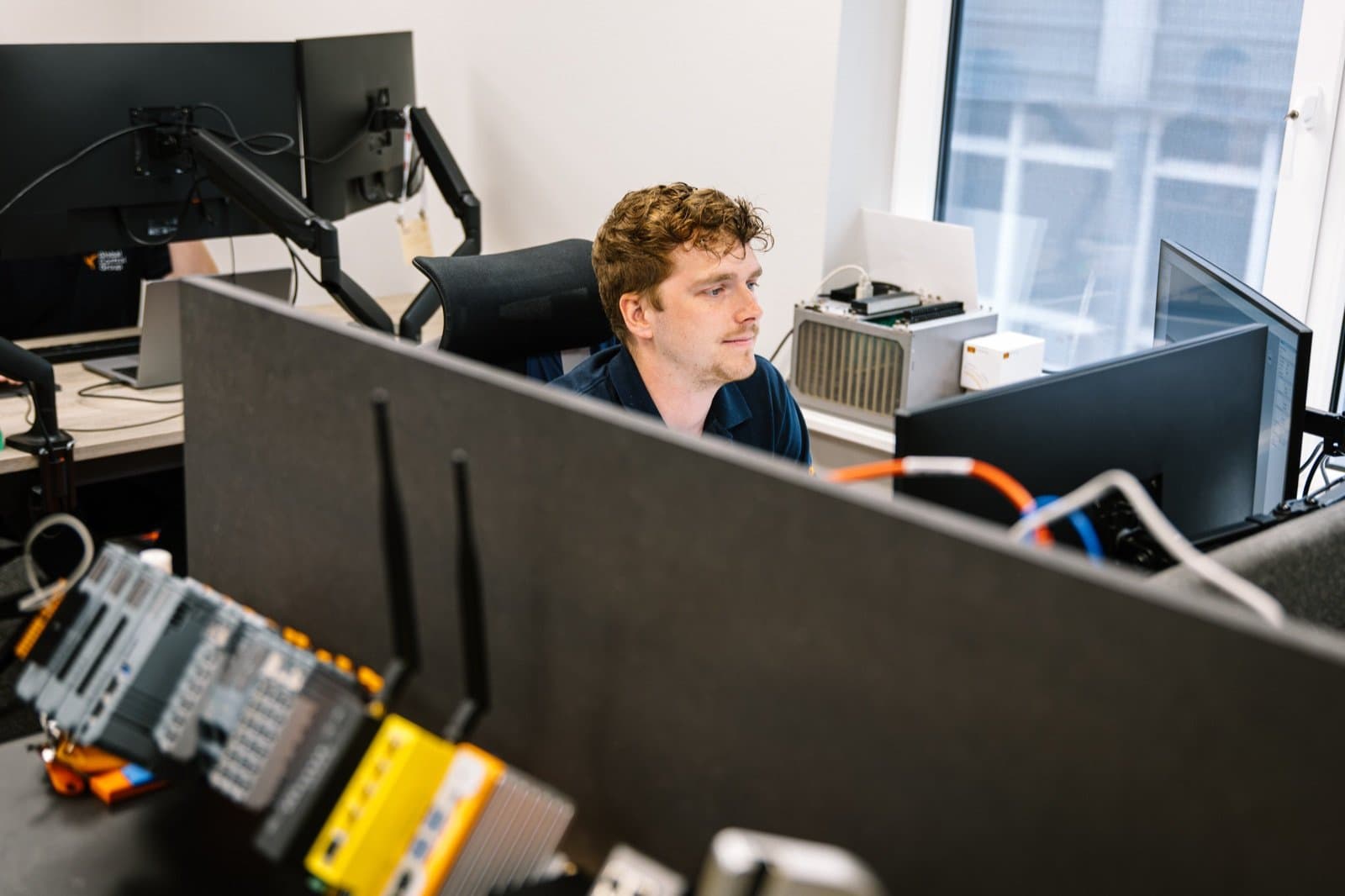 GCG engineer working at an office desk on a PLC programming setup with multiple screens