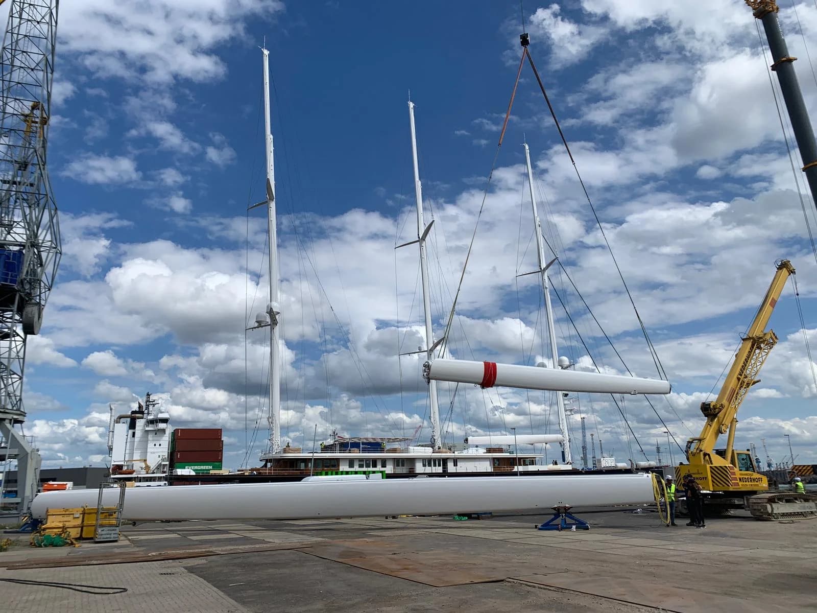Sailing yacht in a harbour, with masts and cranes.